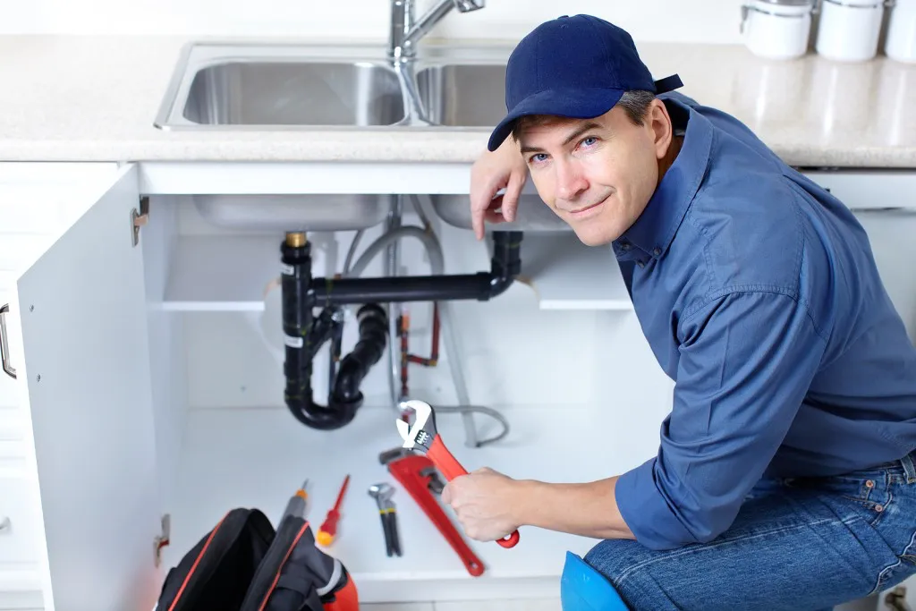 Plumber fixing pipes under a kitchen sink.