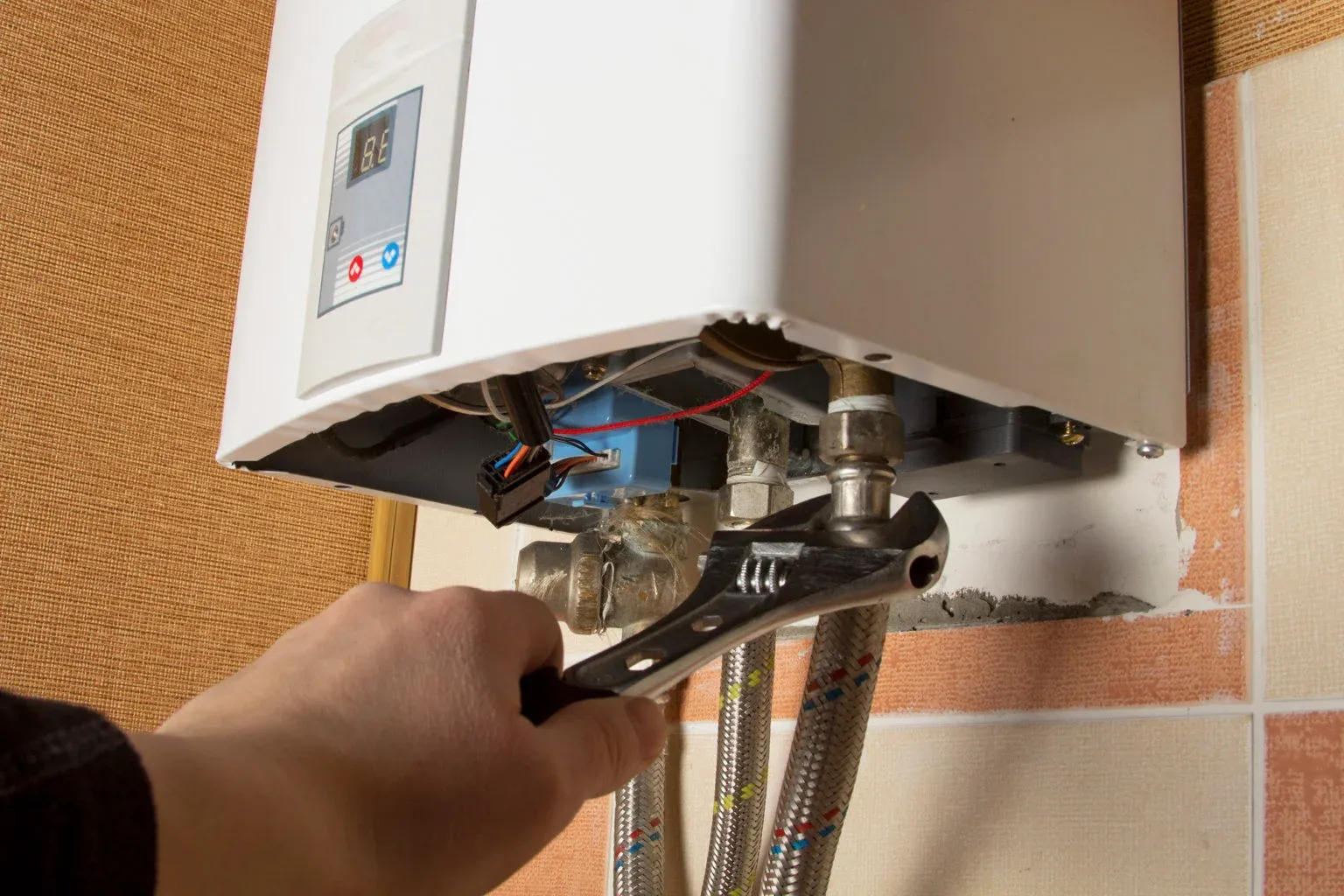 Hand using a wrench to repair a water heater.